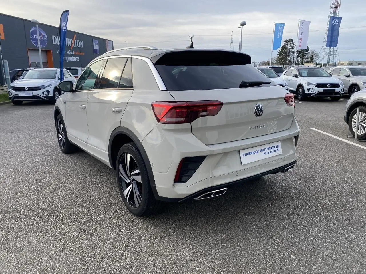 Vue 3/4 arrière droite d'un Volkswagen T-Roc gris clair avec jantes alliage bicolores et vitres arrière teintées.