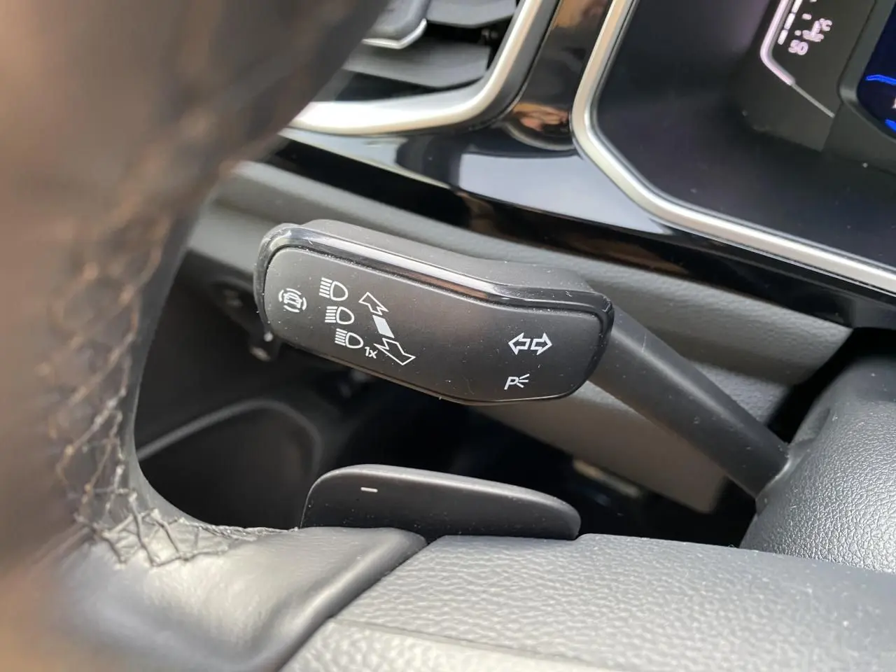 Gros plan sur la manette de clignotant noire à gauche du volant en cuir dans l'habitacle du Volkswagen T-Roc gris.