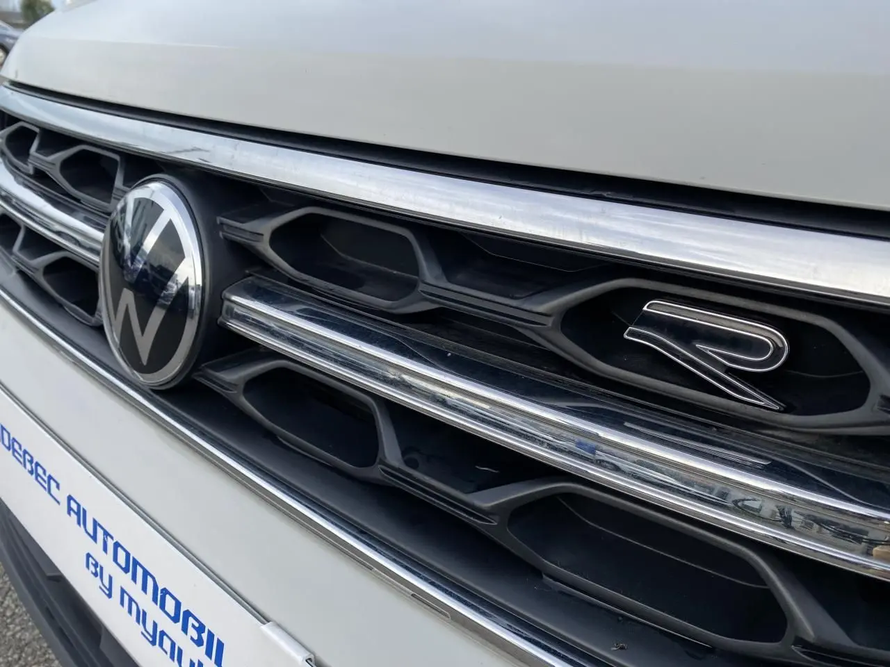 Gros plan sur la calandre avant grise du Volkswagen T-Roc avec logo VW et emblème R visible.