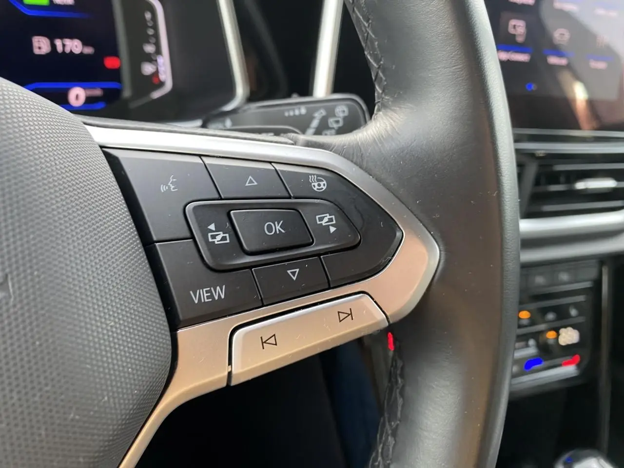 Gros plan sur les commandes gauche du volant cuir noir du Volkswagen T-Roc 2024 avec boutons multifonctions.