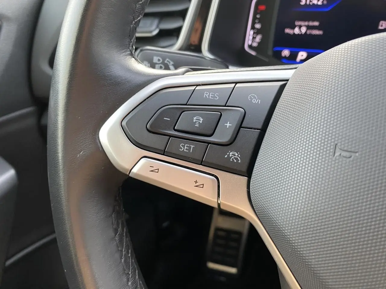 Gros plan sur les commandes à gauche du volant en cuir noir du Volkswagen T-Roc 2024 avec affichage digital en arrière-plan.