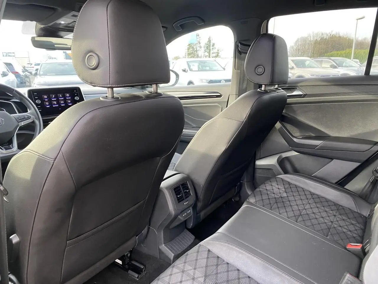 Vue intérieure arrière du Volkswagen T-Roc 2024 gris, montrant les sièges avant en similicuir noir et la banquette arrière avec surpiqûres.