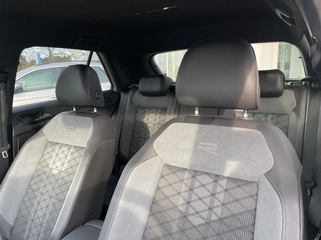 Vue intérieure des sièges avant et arrière du Volkswagen T-Roc 2024 avec sellerie mixte cuir et tissu gris à motif géométrique.