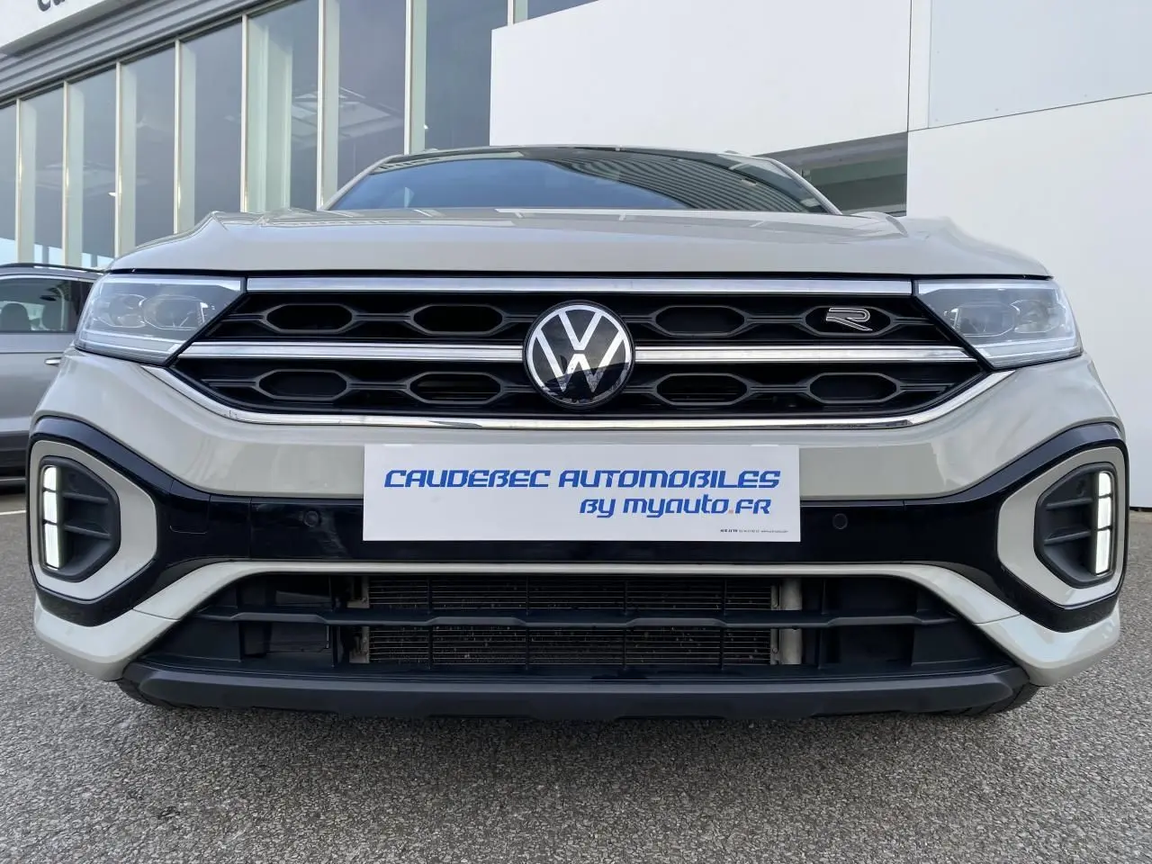 Vue frontale rapprochée du Volkswagen T-Roc gris avec calandre noire et logo R-Line visible sur la grille.