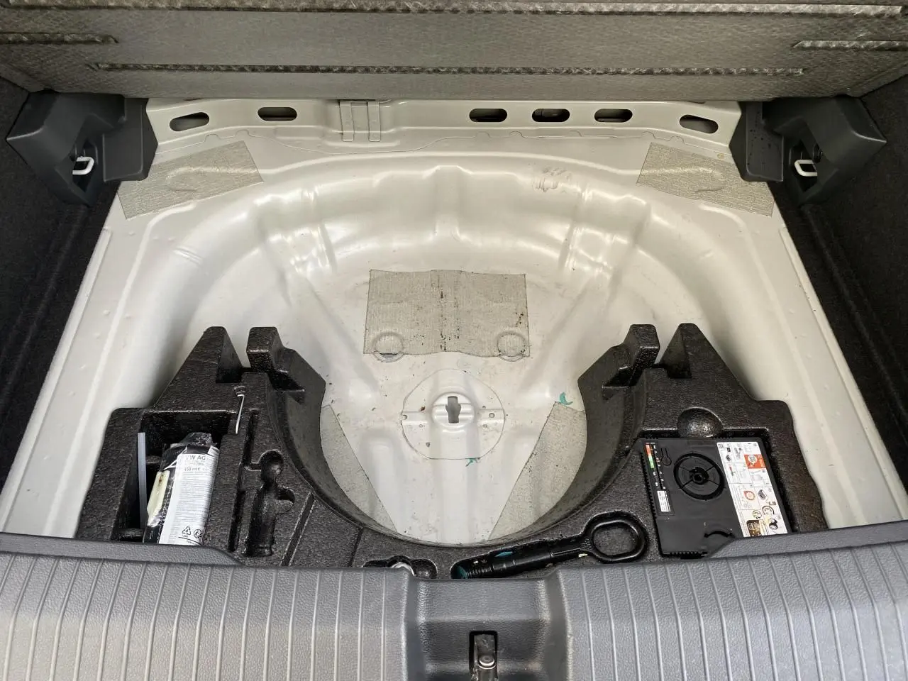 Vue du coffre ouvert d'un Volkswagen T-Roc 2024 gris, montrant le rangement sous plancher sans roue de secours.