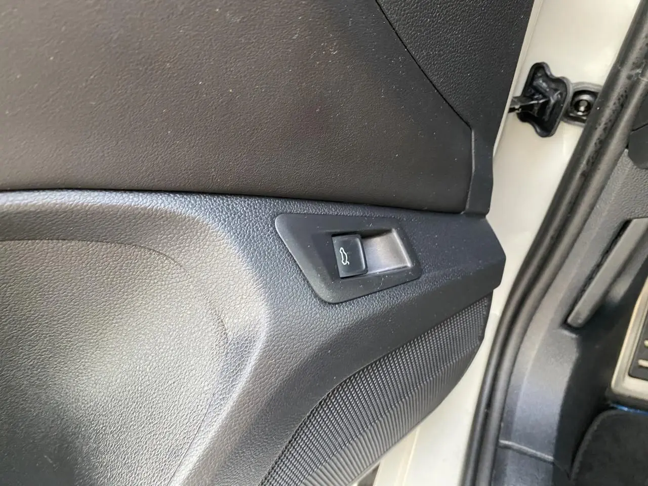 Détail du bouton d'ouverture du coffre sur la porte côté conducteur d'un Volkswagen T-Roc gris 2024.