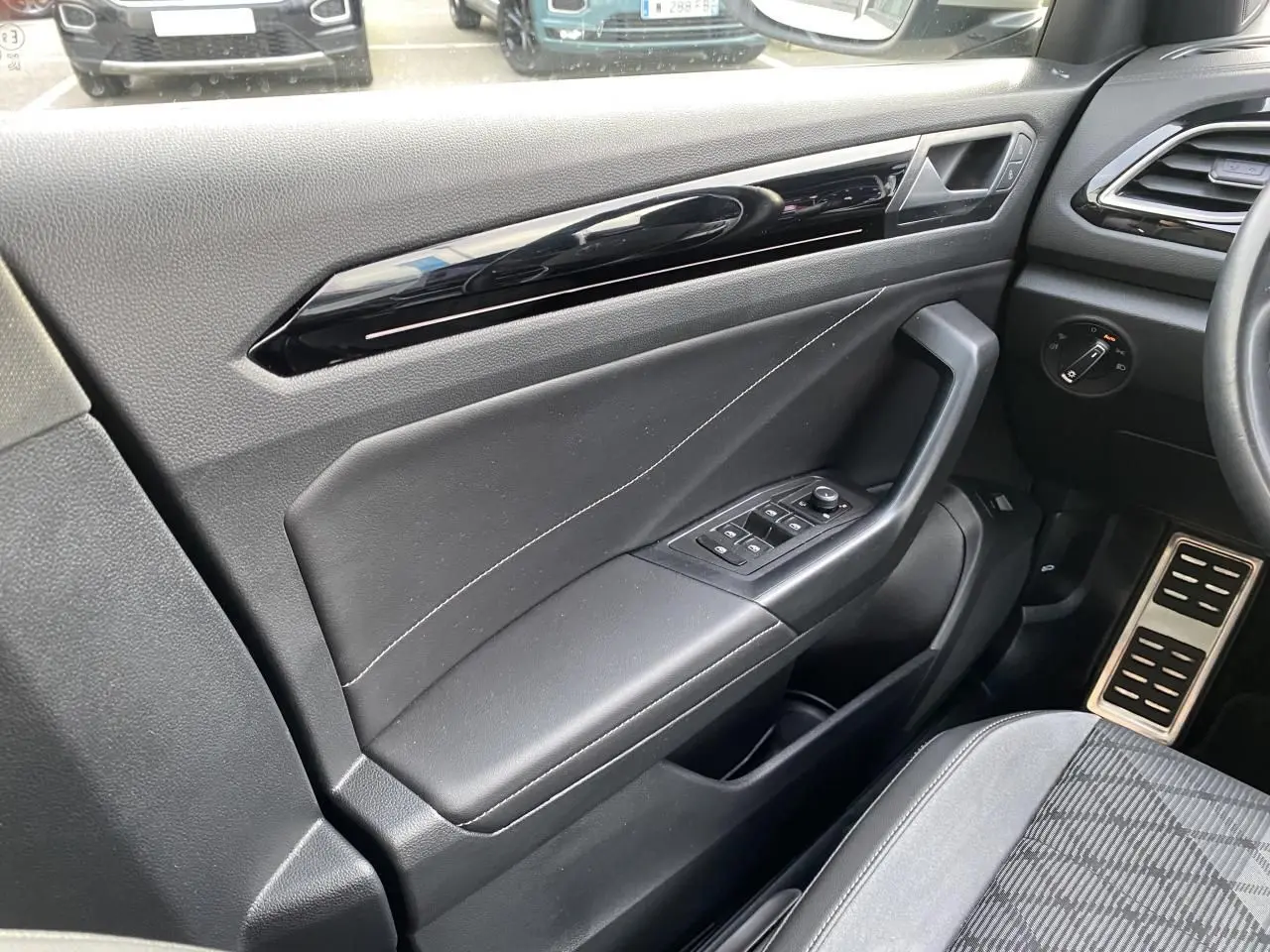 Intérieur côté conducteur du Volkswagen T-Roc 2024, porte noire avec commandes des vitres et pédalier en acier brossé.