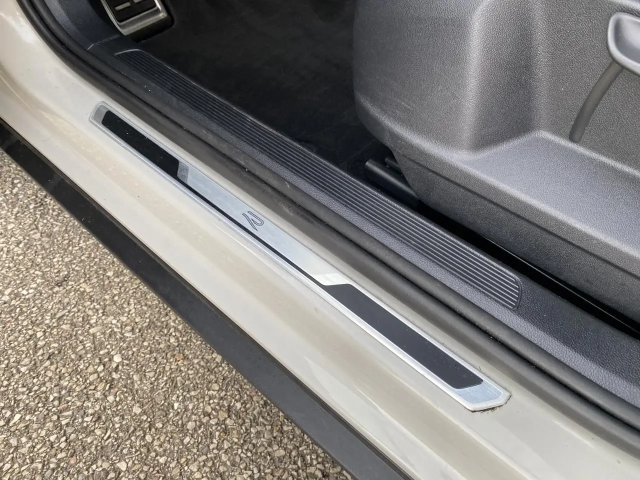 Gros plan sur la plaque de seuil de porte R-Line d'un Volkswagen T-Roc gris, côté conducteur, avec intérieur noir.