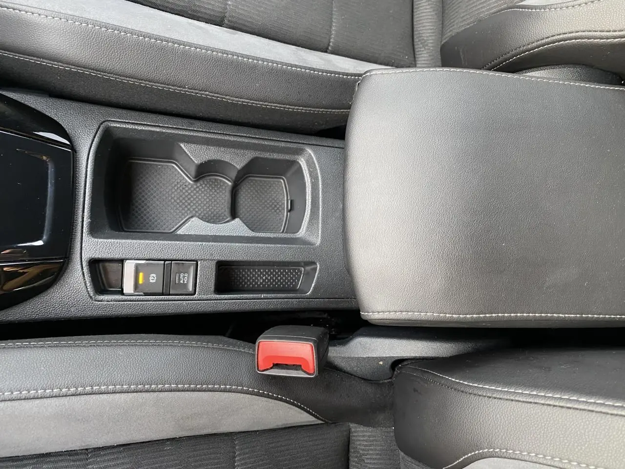 Vue rapprochée de la console centrale grise avec accoudoir en similicuir et bouton frein à main électrique du Volkswagen T-Roc 2024.