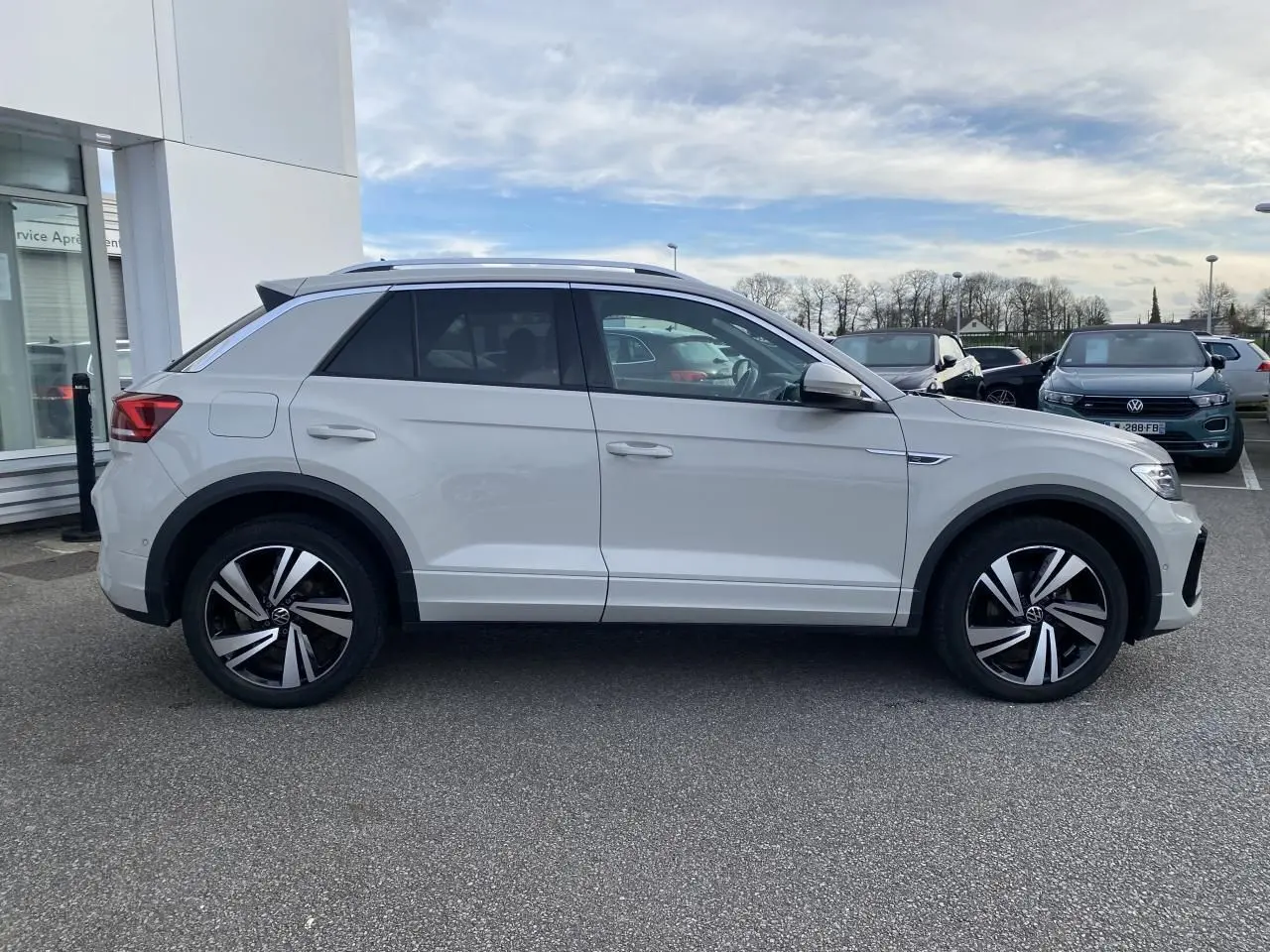 Profil côté gauche d'un Volkswagen T-Roc gris clair 2024 avec jantes alliage bicolores et vitres surteintées.