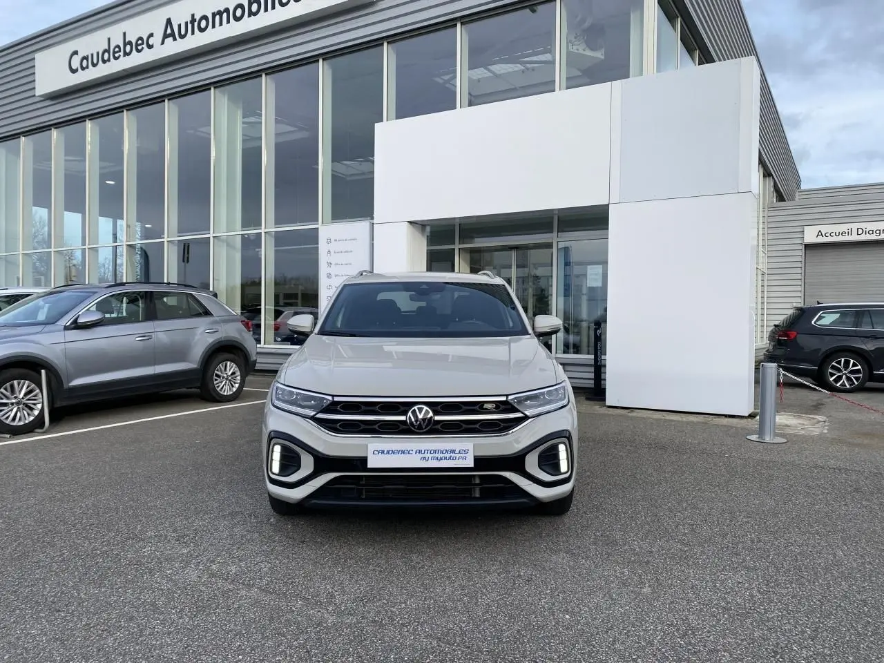 Volkswagen T-Roc gris vue de face, avec calandre noire et feux LED, stationné devant un showroom.