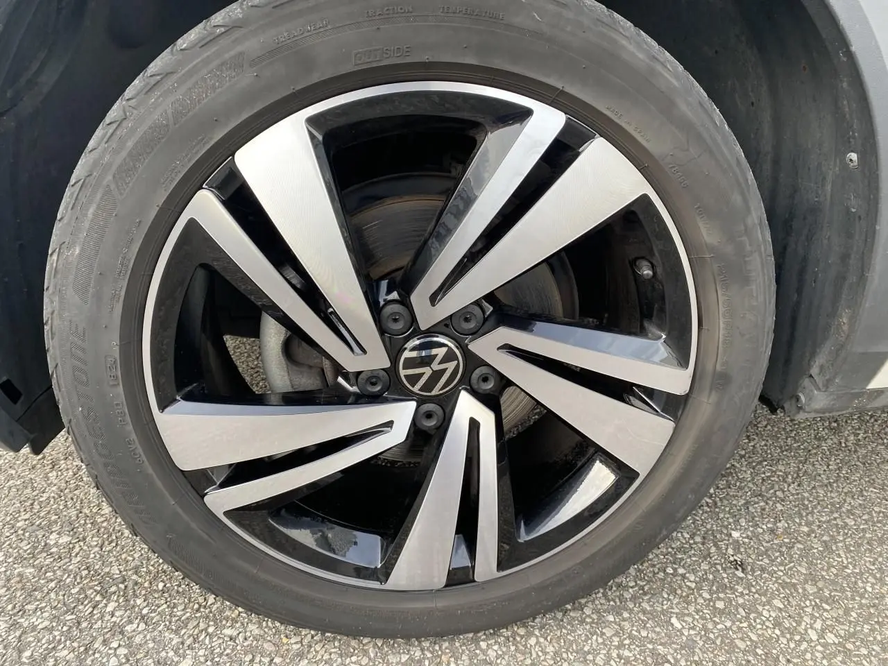 Gros plan sur la jante en alliage léger Nevada noire et brillante du côté avant droit d'un Volkswagen T-Roc gris.