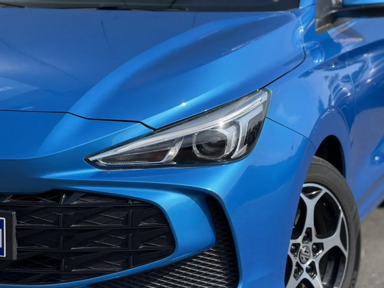 Gros plan sur l'avant droit bleu Como du MG3 1.5 Hybrid+ 195 Comfort, avec phare LED et calandre noire ajourée.