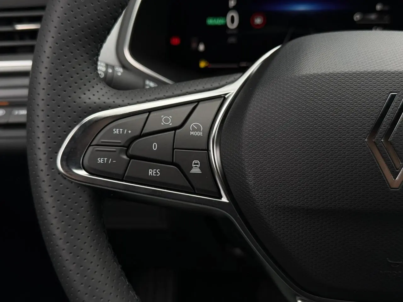 Gros plan sur le côté gauche du volant noir perforé du Renault Captur 2026, avec commandes intégrées et logo central.
