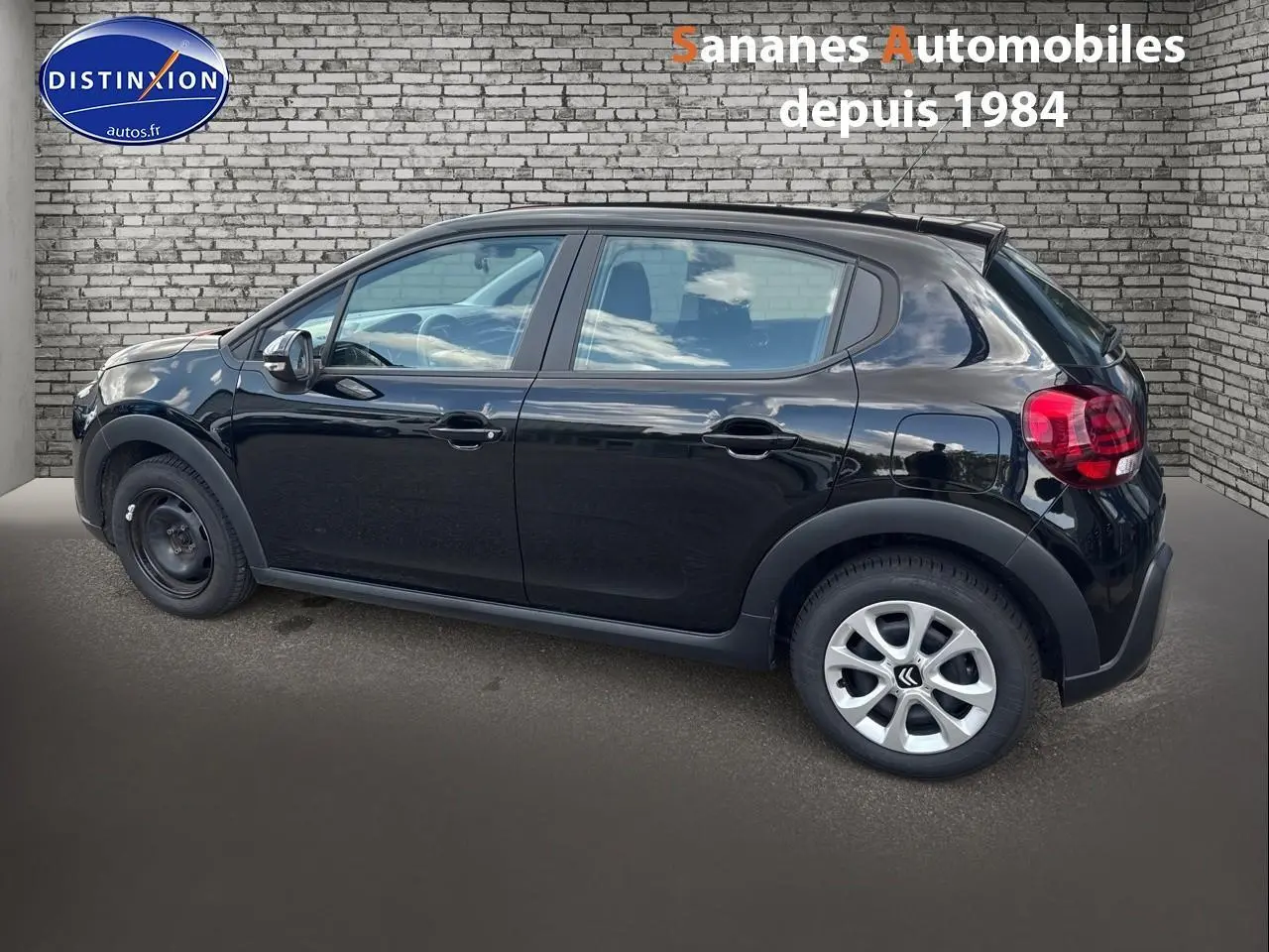 Profil côté gauche d'une Citroën C3 noire 2023 avec jantes alliage arrière et roue acier avant, devant un mur en briques.