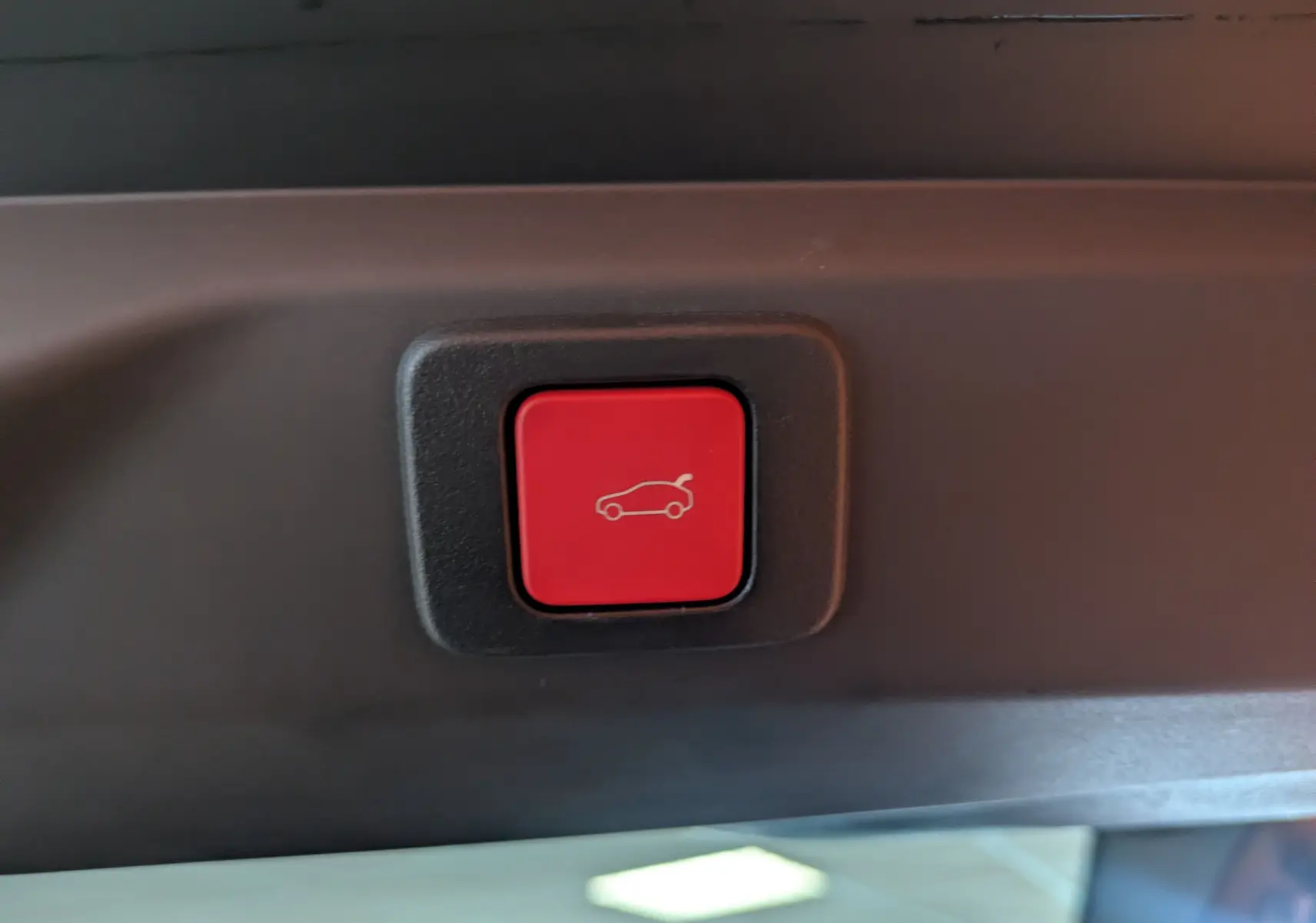 Bouton rouge d'ouverture électrique du hayon du Peugeot 3008 blanc, gros plan intérieur sur la porte arrière.