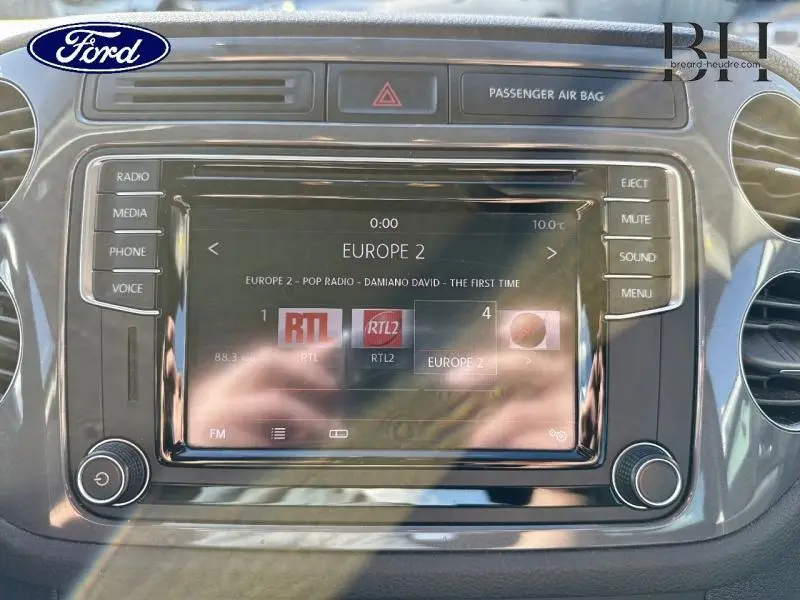 Vue rapprochée de l’écran tactile multimédia du Volkswagen Tiguan gris Crypton, avec commandes audio et affichage radio Europe 2.
