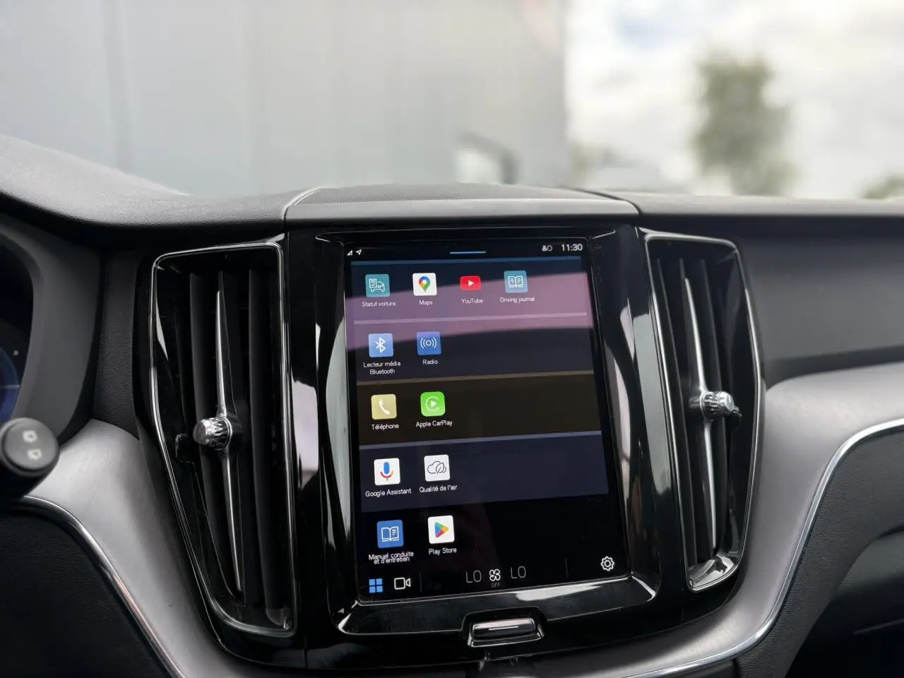 Vue rapprochée de l’écran tactile central du tableau de bord du Volvo XC60 rouge, entouré de deux aérateurs verticaux noirs.