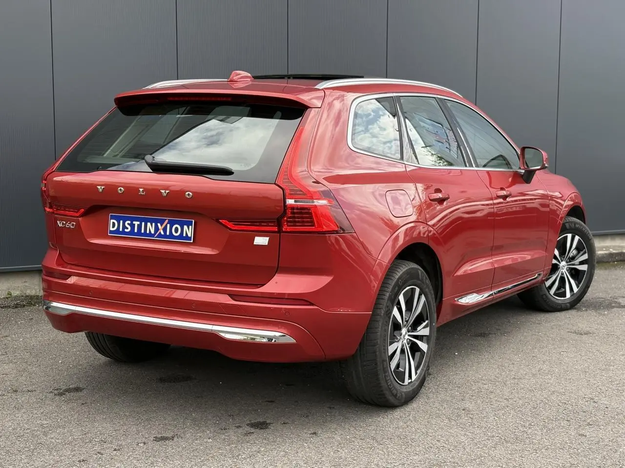 Vue 3/4 arrière droite du Volvo XC60 rouge Fusion 2024 avec jantes alliage et contours chromés des vitres.