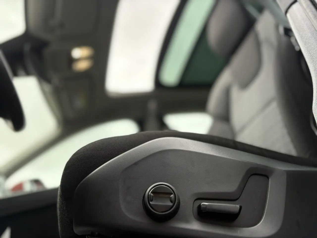 Détail des commandes de réglage électrique du siège avant côté conducteur dans un Volvo XC60 rouge Fusion 2024.