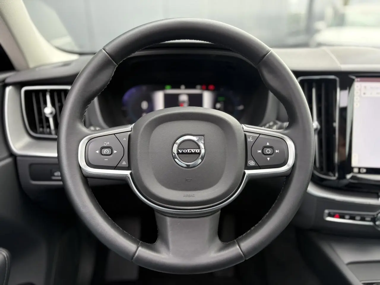 Volant simili-cuir noir de Volvo XC60 2024 vu de face avec commandes intégrées et tableau de bord digital flou.