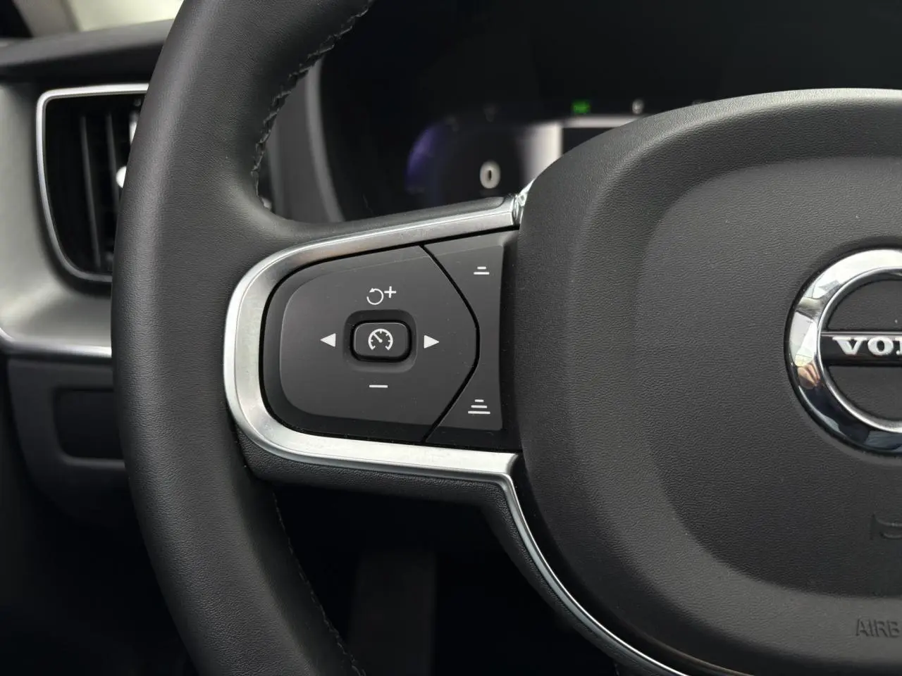 Gros plan sur la partie gauche du volant noir simili-cuir du Volvo XC60 2024 avec commandes de régulateur de vitesse.