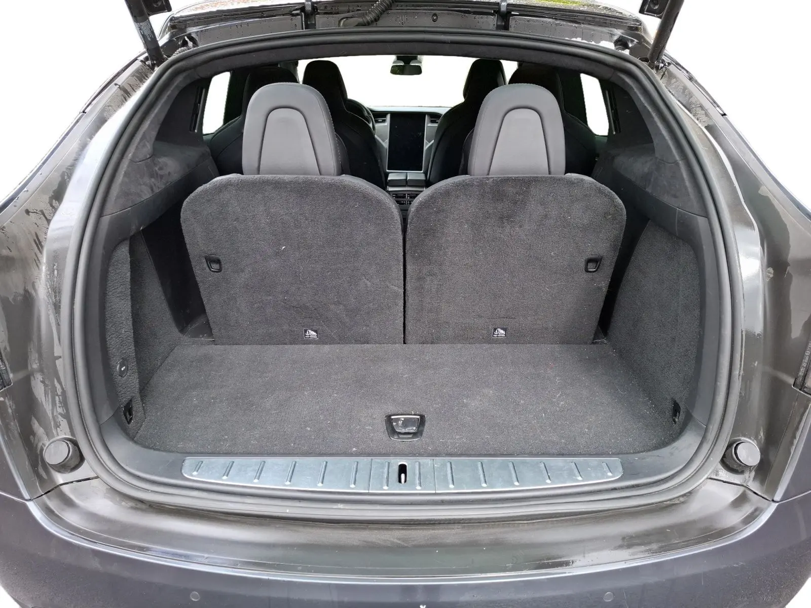 Vue arrière du coffre ouvert d’un Tesla Model X 100D gris foncé, montrant les sièges arrière et l’intérieur spacieux.