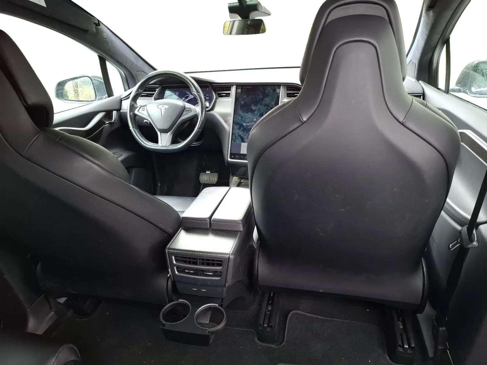 Vue intérieure arrière du Tesla Model X 100D gris foncé, montrant les sièges avant en cuir et l'écran tactile central vertical.