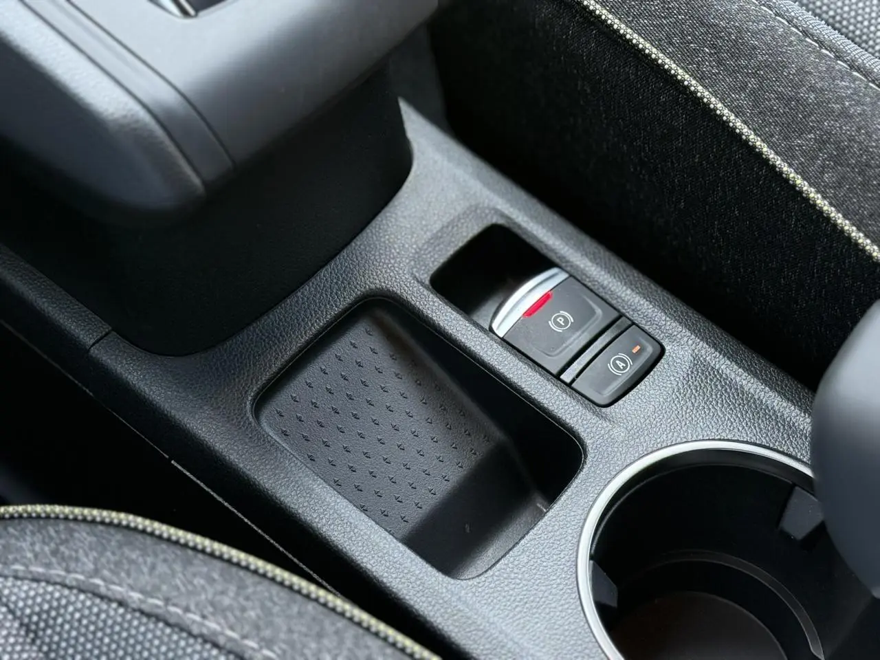 Gros plan sur la console centrale noire du Renault Captur gris Cassiopée, avec frein à main électrique et rangement.