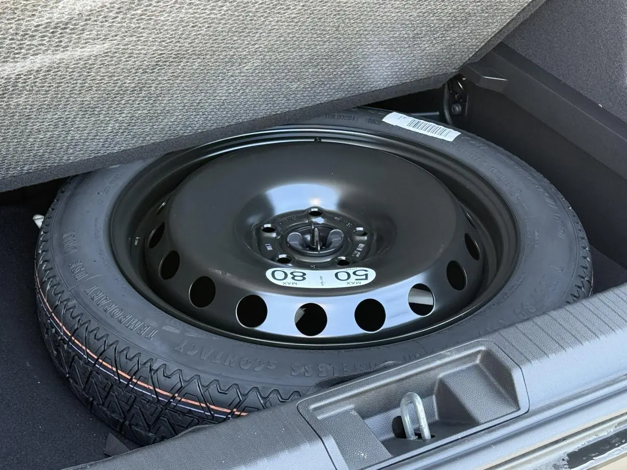 Roue de secours temporaire noire dans le coffre du Renault Captur gris Cassiopée, vue rapprochée du pneu sous plancher.
