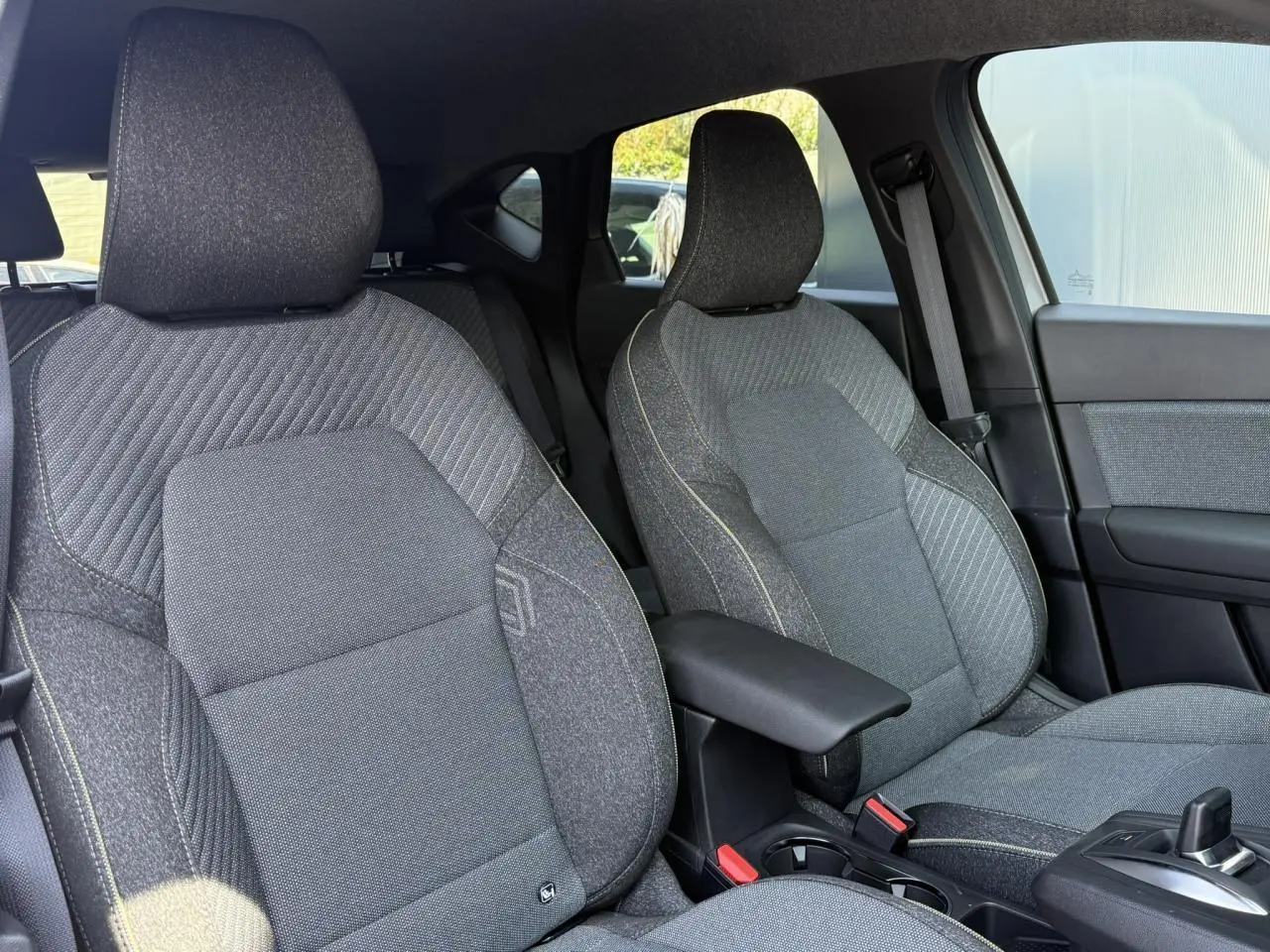 Vue intérieure sur les sièges avant gris texturés du Renault Captur 2026 avec accoudoir central et console de boîte auto.