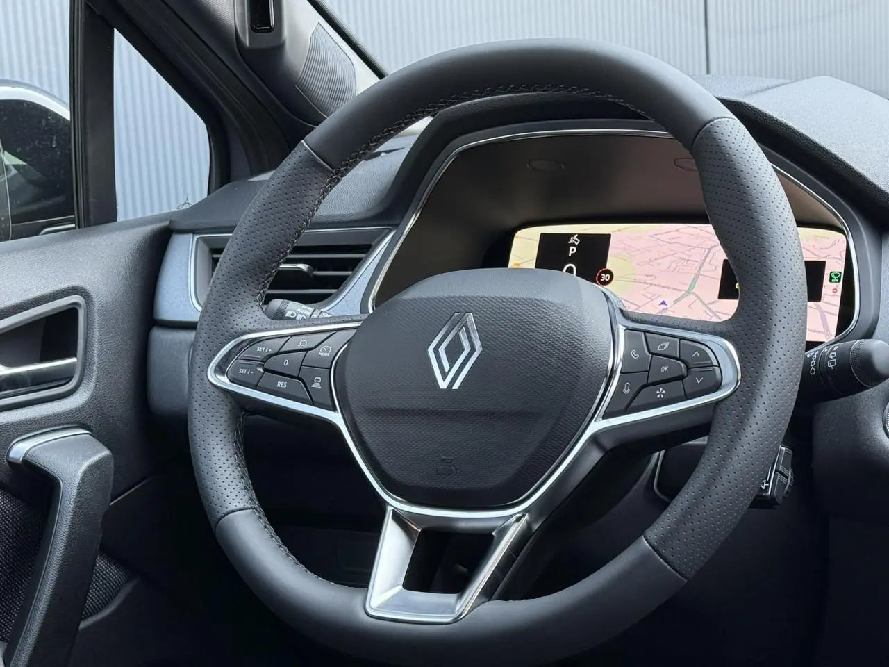 Vue rapprochée du volant noir perforé du Renault Captur 2026 avec tableau de bord numérique et navigation affichée.