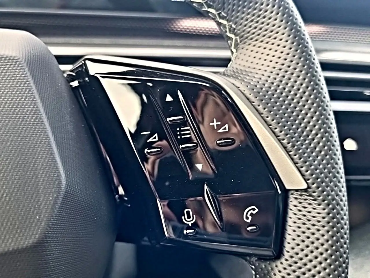 Gros plan sur les commandes noires du volant cuir perforé côté gauche du Peugeot 5008 Hybrid 145 GT e-DCS6.