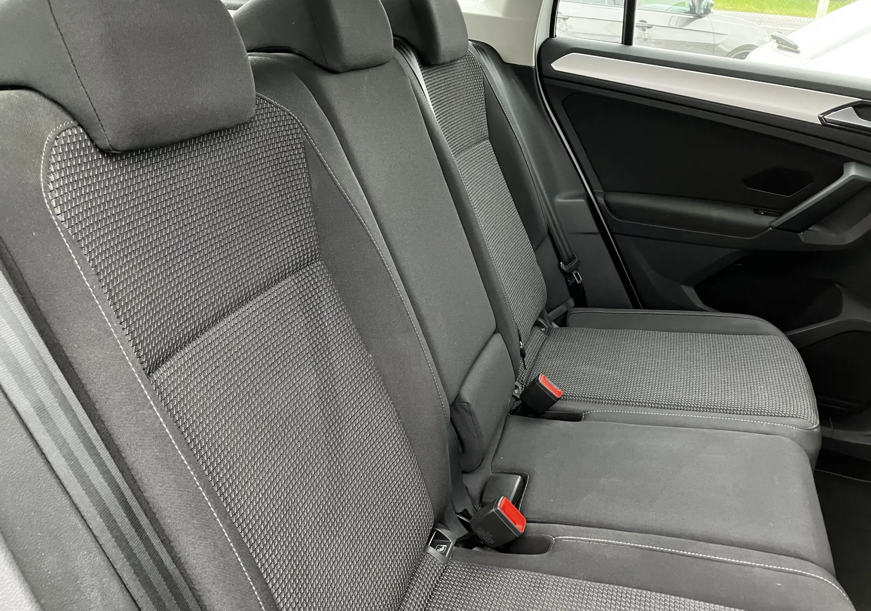 Vue latérale des sièges arrière noirs en tissu du Volkswagen Tiguan blanc 2018, soulignant les ceintures de sécurité et appuie-têtes.