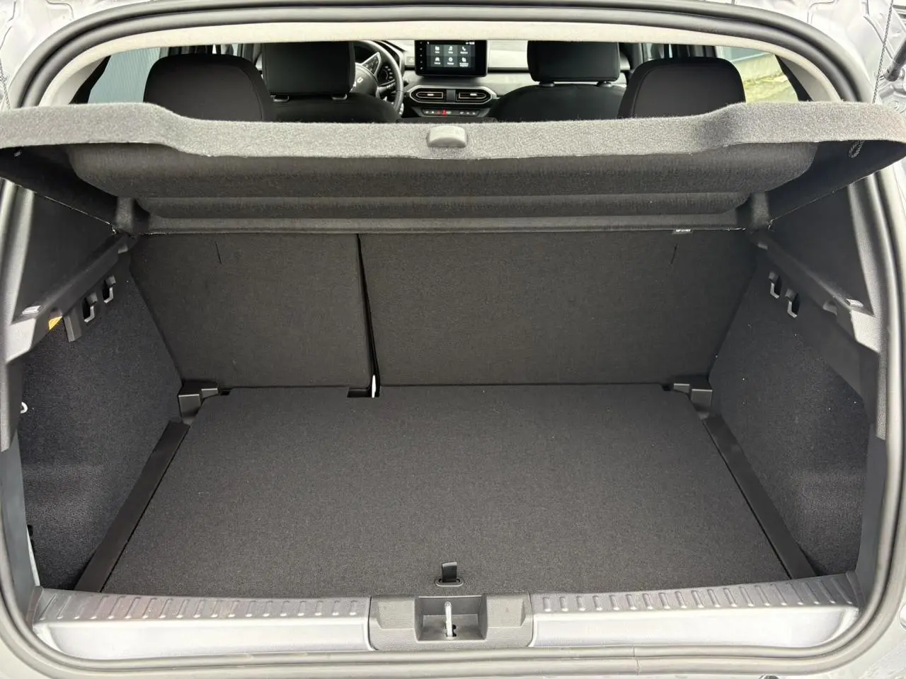 Coffre ouvert de la Dacia Sandero Stepway gris schiste, montrant l'espace de chargement et la banquette arrière rabattable.