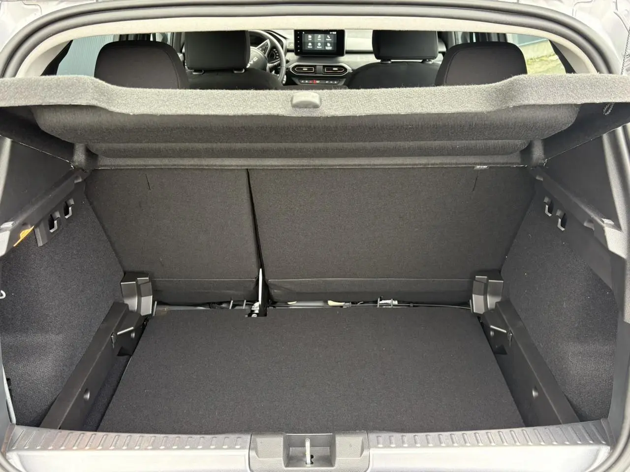 Coffre ouvert vu de l'arrière d'une Dacia Sandero Stepway 2025, intérieur noir avec tablette de coffre relevée.