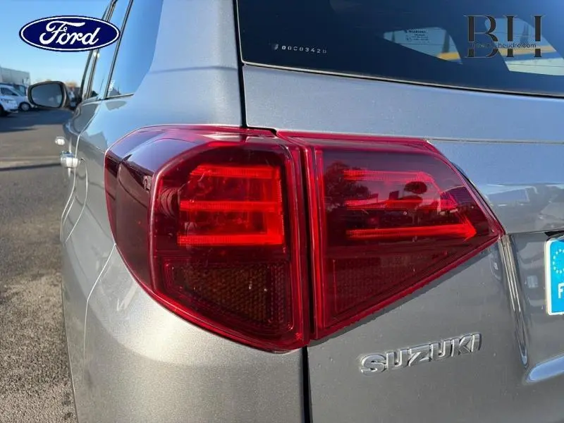 Gros plan sur le feu arrière gauche d'un Suzuki Vitara Galactic Gray métallisé, avec logo et partie de la carrosserie visible.