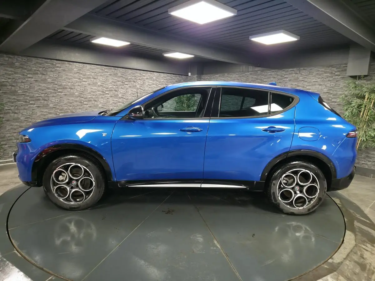 Profil latéral gauche de l'Alfa Romeo Tonale 1.3 PHEV bleu métallisé avec rétroviseurs noirs brillants en intérieur.