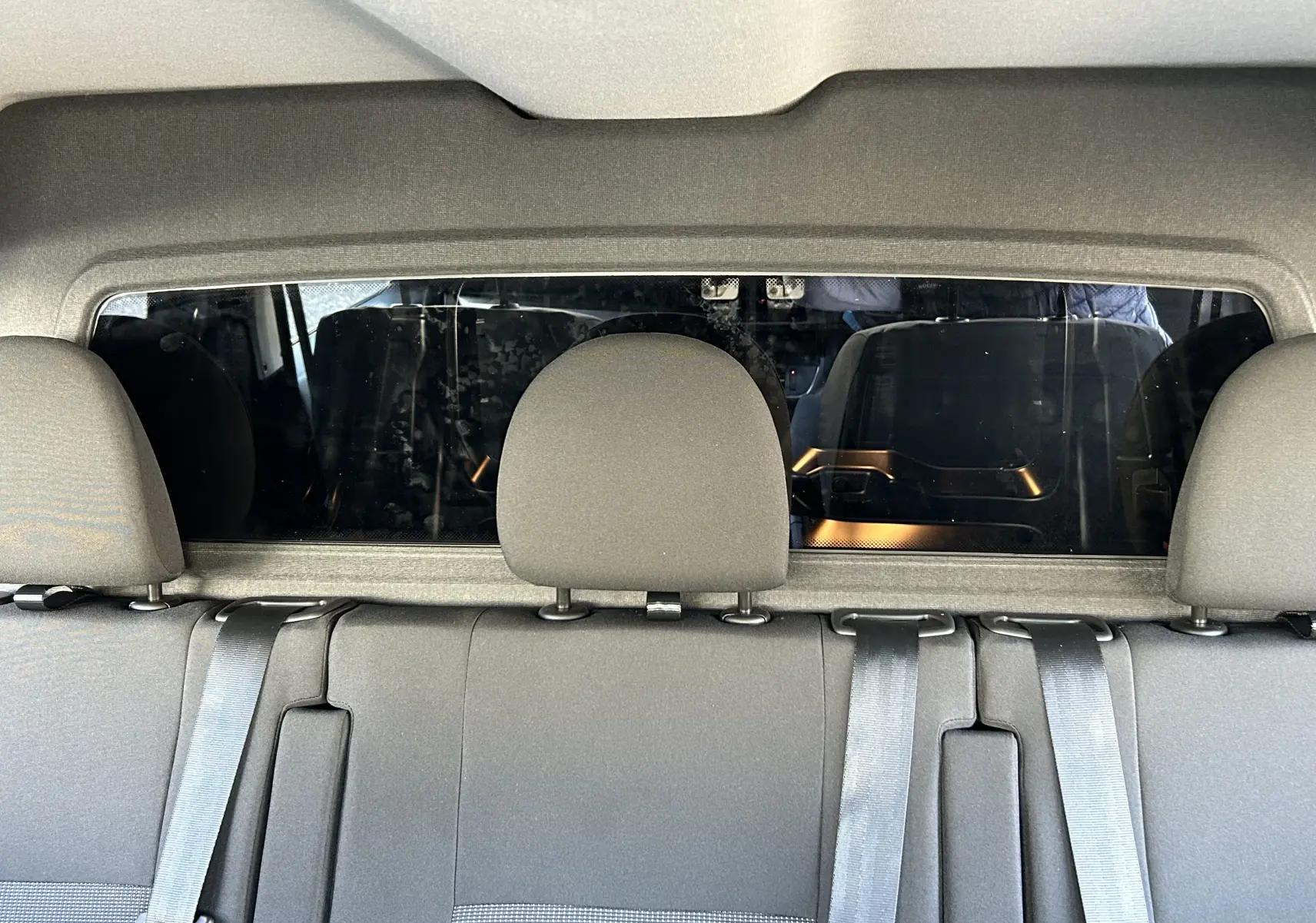 Vue intérieure arrière des sièges gris du Citroën Jumpy Cabine Approfondie noir, avec ceinture de sécurité et vitre séparatrice.