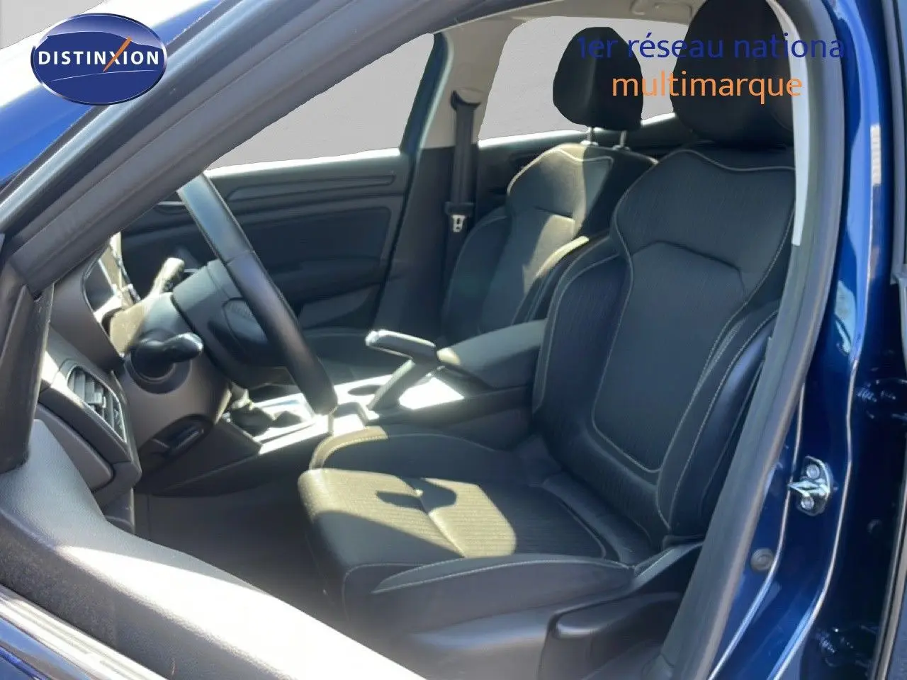 Vue intérieure côté conducteur de la Renault Mégane bleu cosmos, sièges noirs en tissu avec surpiqûres blanches.