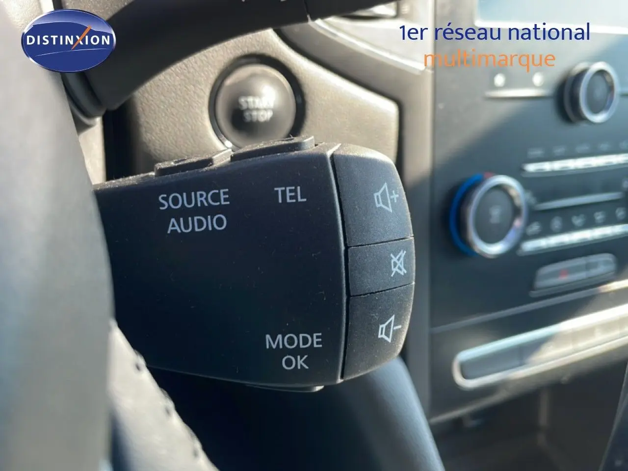 Gros plan sur la commande audio au volant d’une Renault Mégane bleu cosmos métal, intérieur noir visible en arrière-plan.