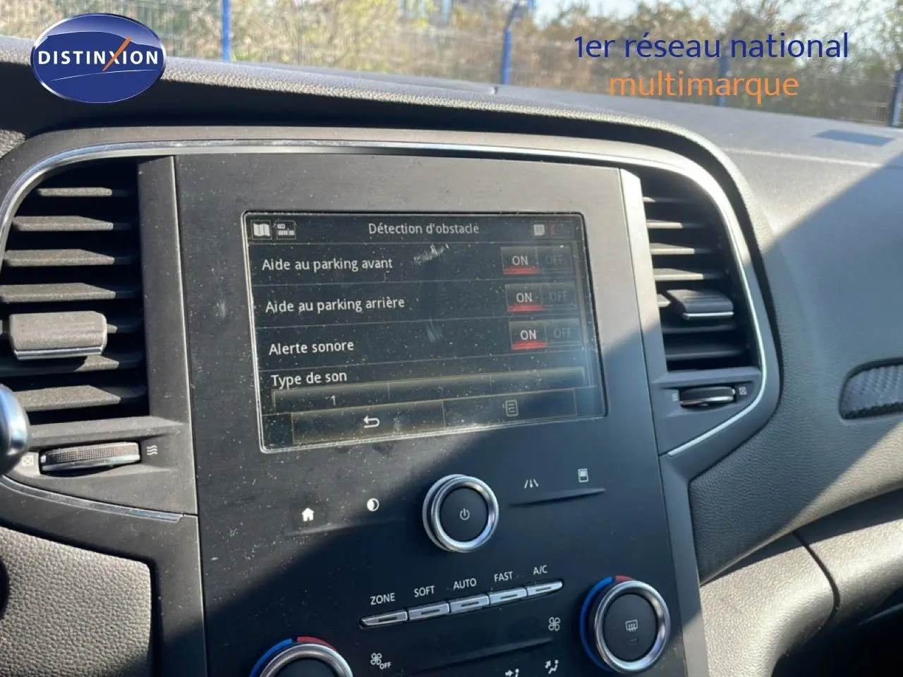 Vue rapprochée de la console centrale d’une Renault Mégane bleu cosmos métal, affichant les réglages d’aide au parking.