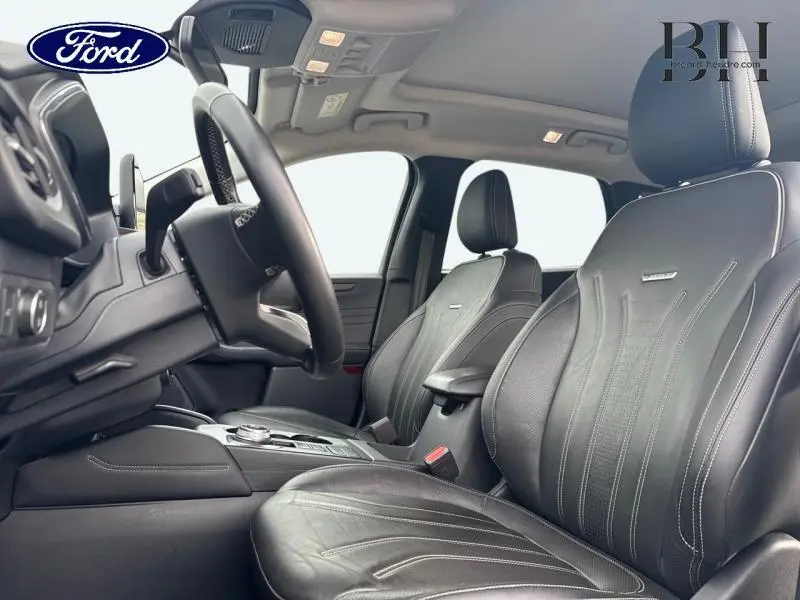Vue intérieure côté conducteur du Ford Kuga 2023, sièges sport cuir noir Windsor avec surpiqûres blanches et volant multifonction.