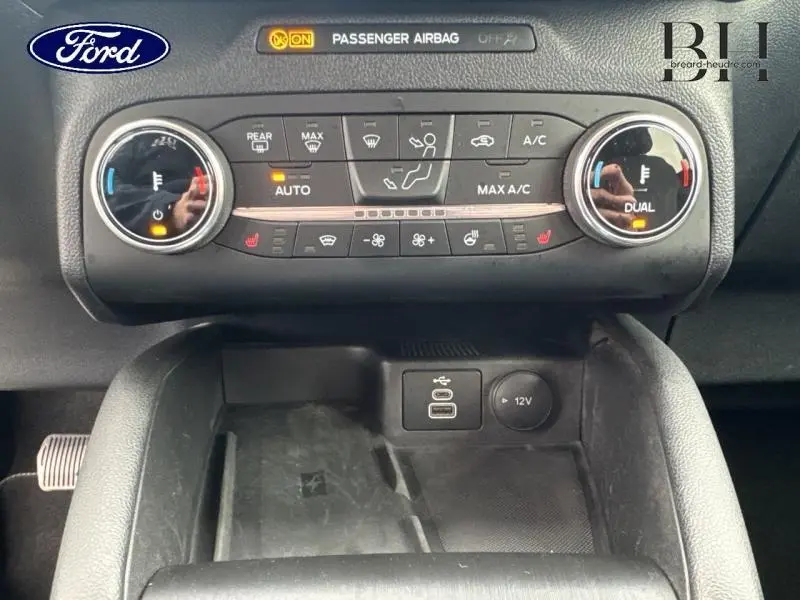 Vue rapprochée de la console centrale du Ford Kuga 2023, avec commandes climatisation bi-zone et prises USB et 12V.