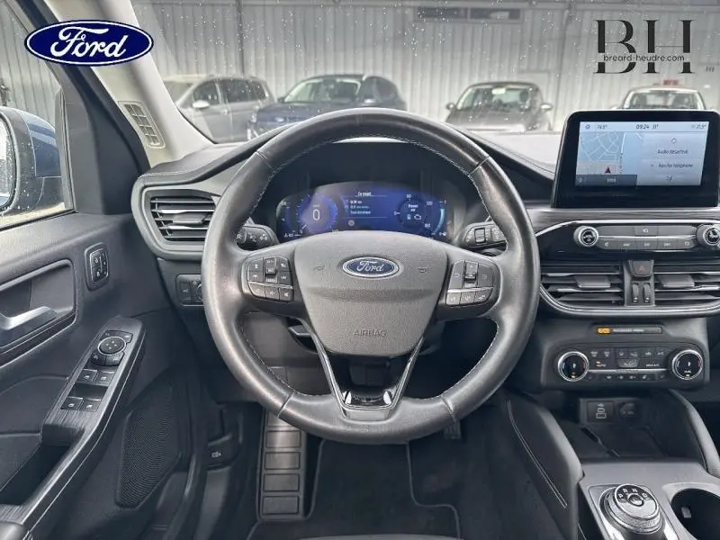 Vue intérieure centrée sur le volant cuir multifonction noir du Ford Kuga 2023 avec tableau de bord digital et écran tactile.