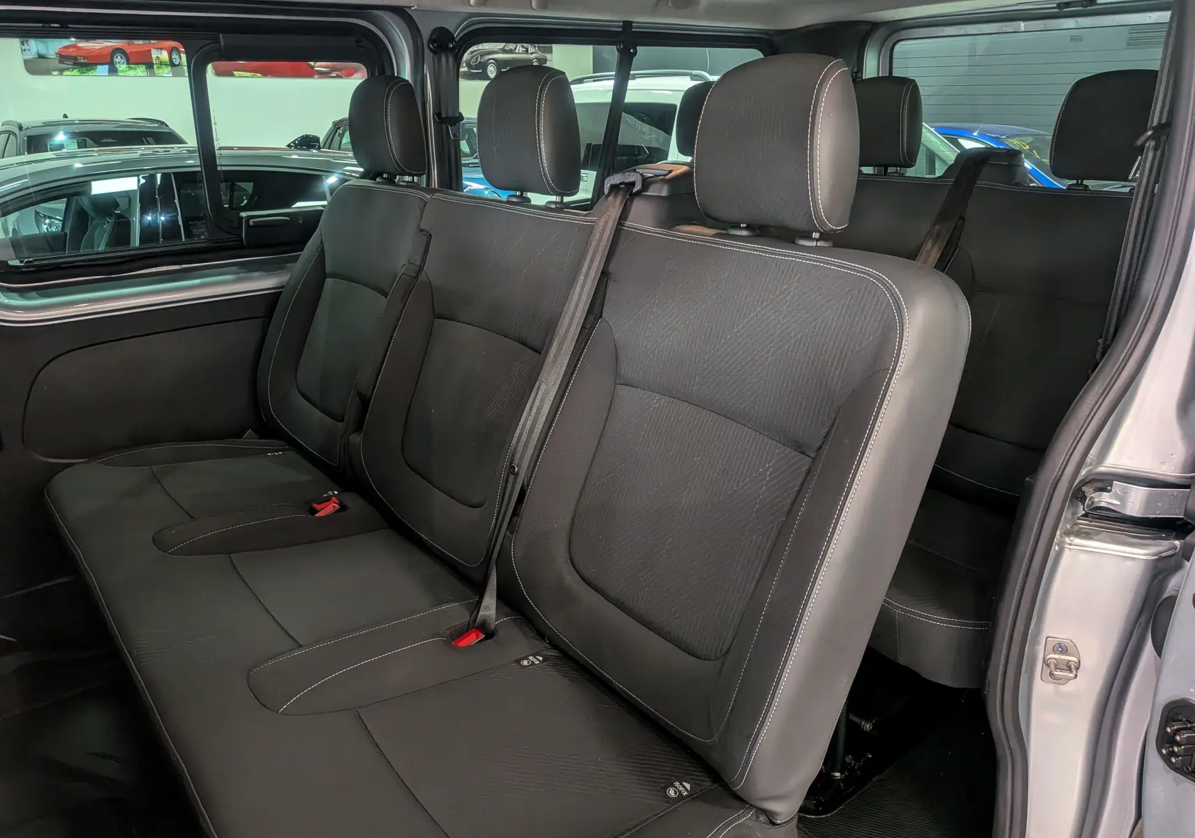 Vue intérieure des sièges arrière en tissu noir du Nissan Primastar Combi gris Highland, avec ceinture de sécurité visible.