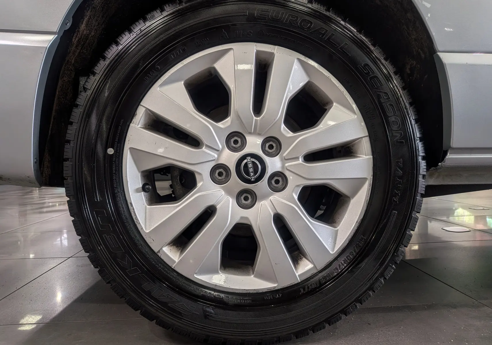 Gros plan sur la roue avant droite du Nissan Primastar Combi gris Highland, jante alliage 17 pouces avec logo Nissan central.