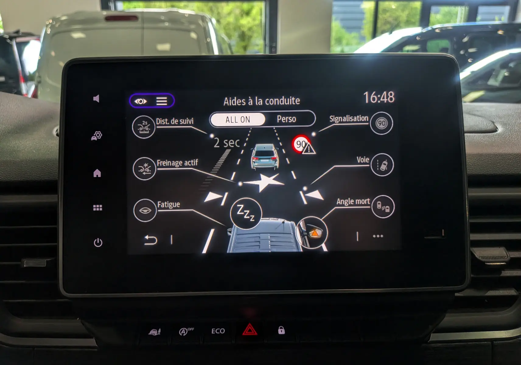 Vue de face de l’écran tactile du Nissan Primastar Combi gris Highland, affichant les aides à la conduite actives.