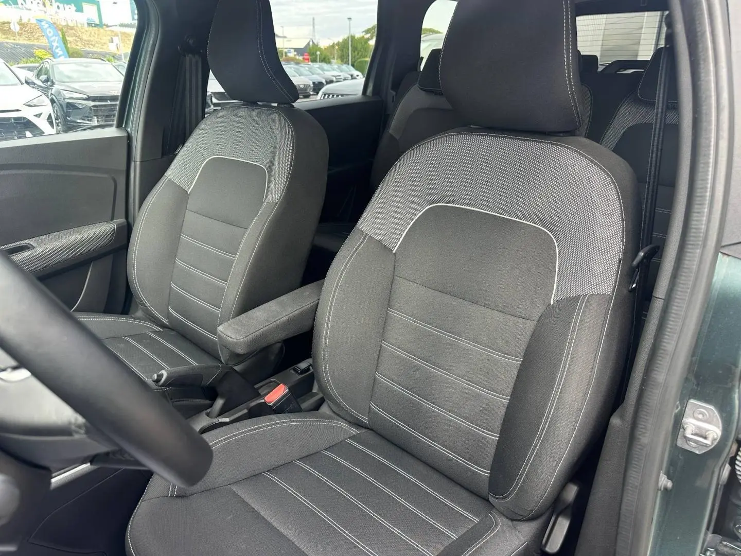 Vue rapprochée des sièges avant en tissu gris du Dacia Jogger vert cèdre, avec accoudoir central côté droit.
