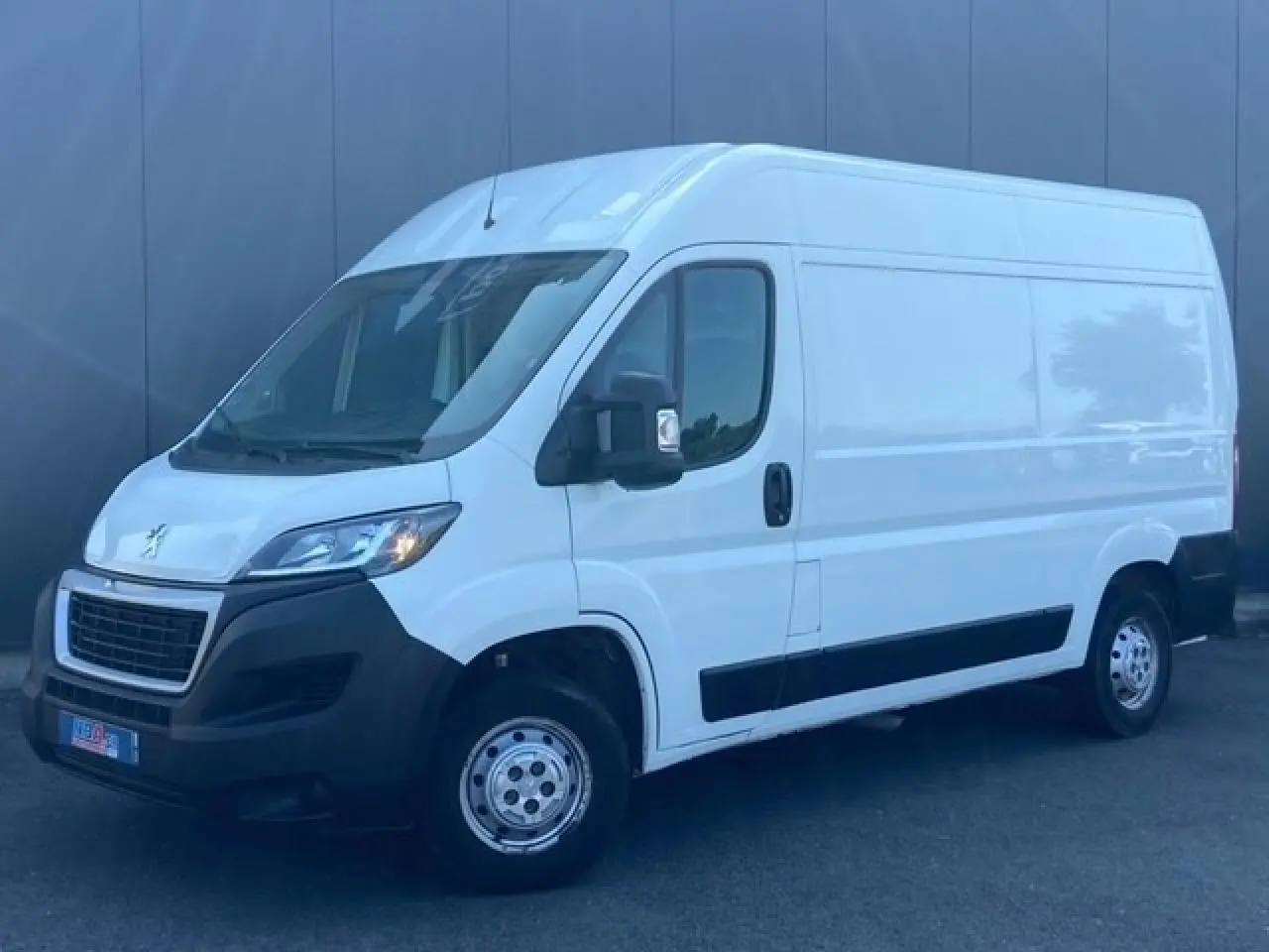 Vue 3/4 avant droit d'un Peugeot Boxer Fourgon blanc de 2019 avec pare-chocs noirs et porte latérale coulissante.
